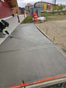 Worker applying broom finish to freshly poured apron concrete in Calgary