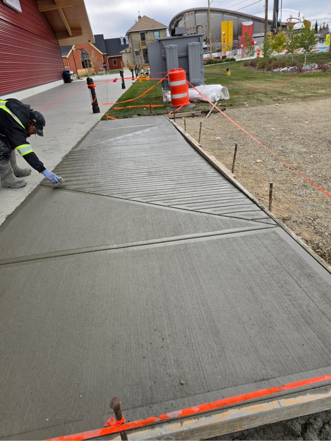 Worker applying broom finish to freshly poured apron concrete in Calgary